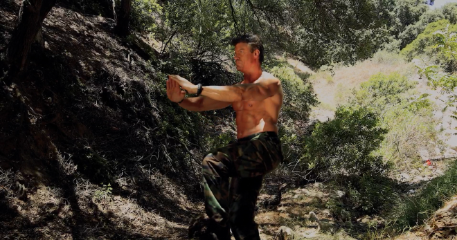 A very fit and muscular man is working out. He is wearing tactical army pants, belt, and boots, but not shirt. He looks very wet and shiny.