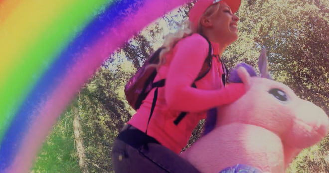 An image of Barbi riding a My Little Pony stuffed animal in the forest. A third of the screen is taken up a rainbow overlay.