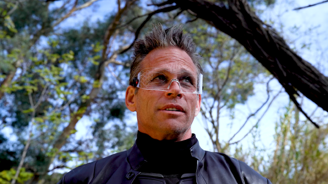 A close-up shot of the character Sklarr. He is a big and tall middle-aged man with spiky hair. He is wearing mostly clear augmented reality glasses and wearing a leather jacket over some kind of body armour.