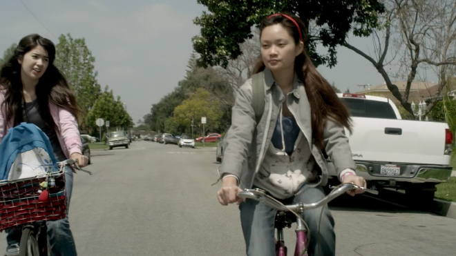 The characters Kayla and Amberlyn biking home on a generic suburban street.