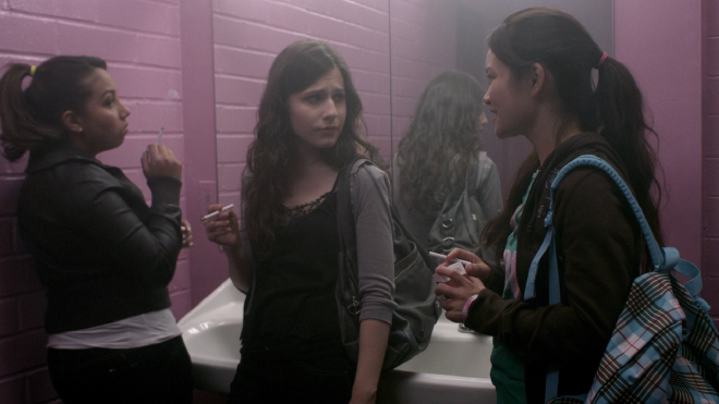 Three girls in what appear to be a school restroom. The two girls on the left are leaning against the sink and smoking cigarettes, while Amberlyn on the right has just pulled a cigarette out and is talking to them.