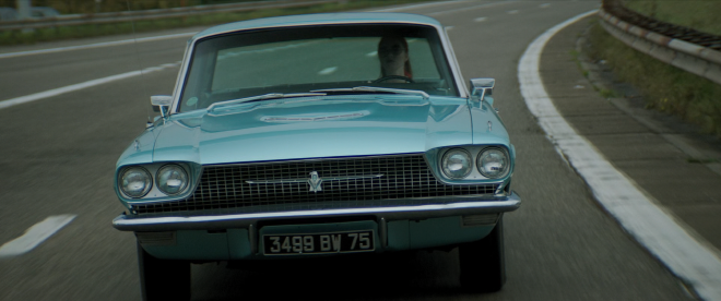 A full shot of the front of a classic teal Thunderbird car that Dany is driving down the highway.