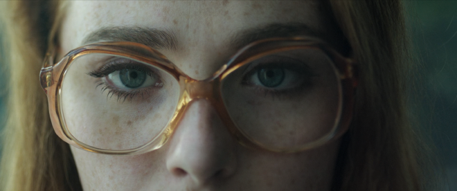 A close up shot of the character Dany putting her glasses on in front of mirror.